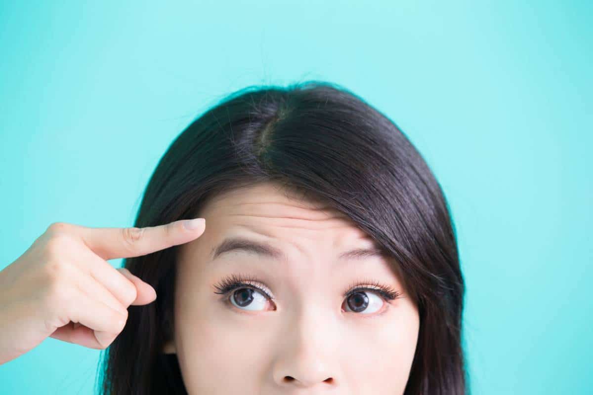 woman against teal background pointing at forehead wrinkles